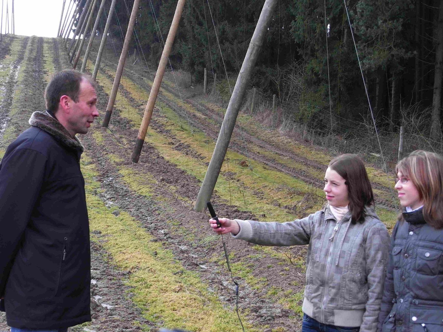 Zwei Mädchen interviewen in einem Hopfengarten einen Hopfenfachmann